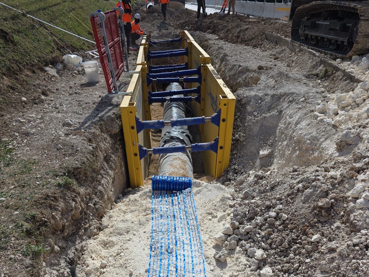 Pipeline installation in a shored trench, with crew and excavator on site