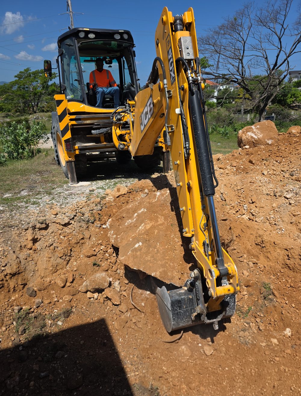 Roots & Rise JCB backhoe loader on an active earthworks site in Jamaica